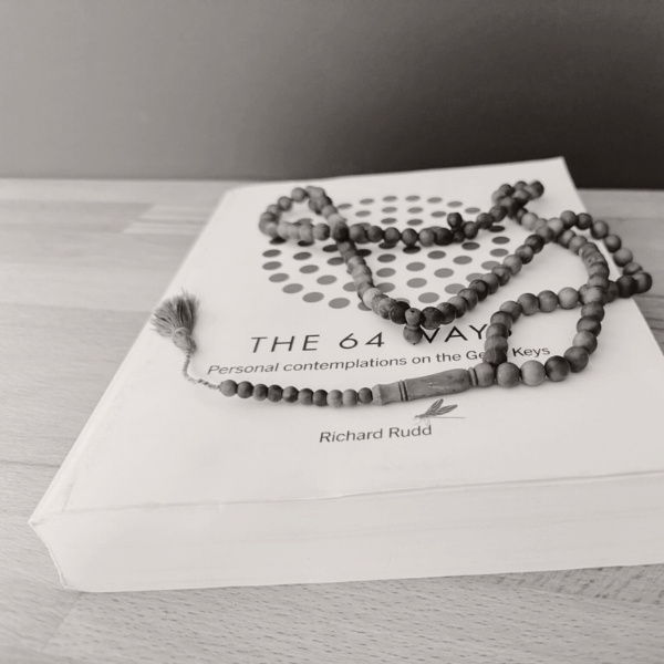 Ein Exemplar von The 64 Ways von Richard Rudd mit einer Mala-Kette – Symbol für kontemplativen Zugang zu Spiritualität und innerem Wissen.